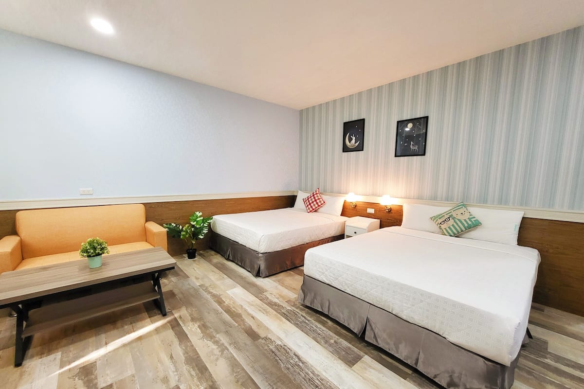 A hotel room with two single beds, a sofa, a small table, and a potted plant.