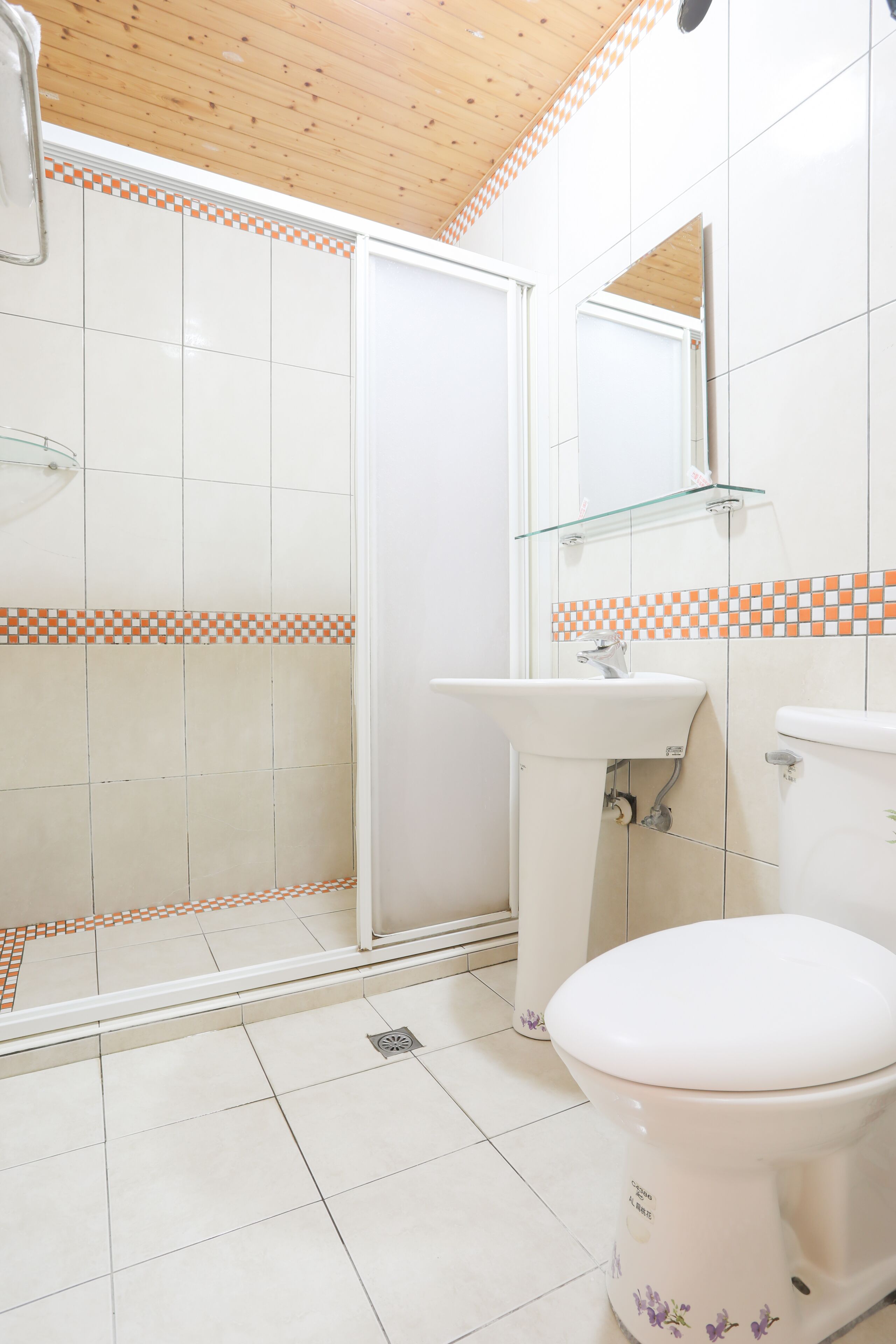 A bathroom with a shower, sink, toilet, and a glass shelf.