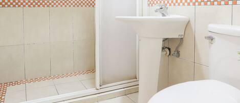 A bathroom with a shower, sink, toilet, and a glass shelf.
