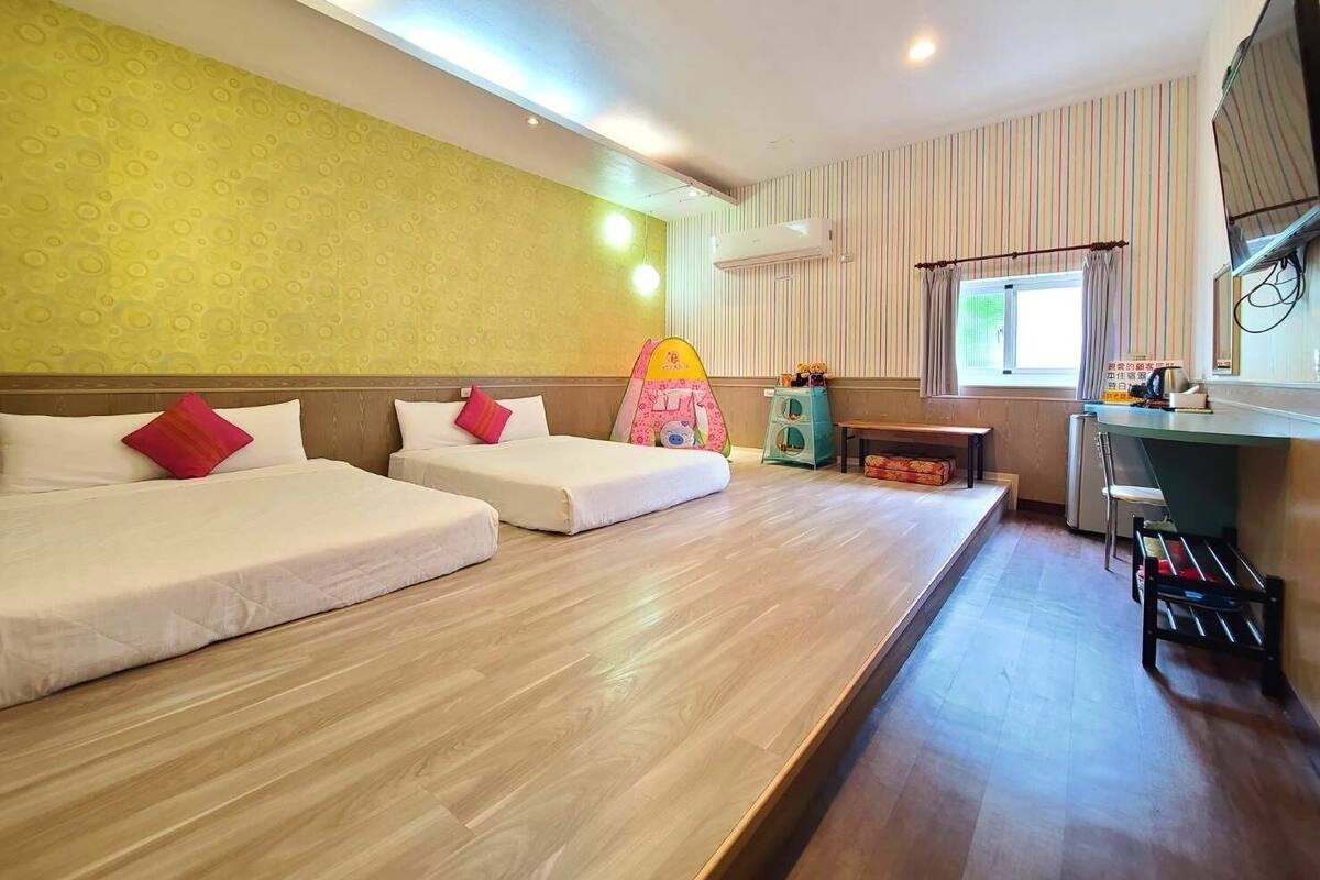 A hotel room with two single beds, a small desk, a television, and a window with curtains.