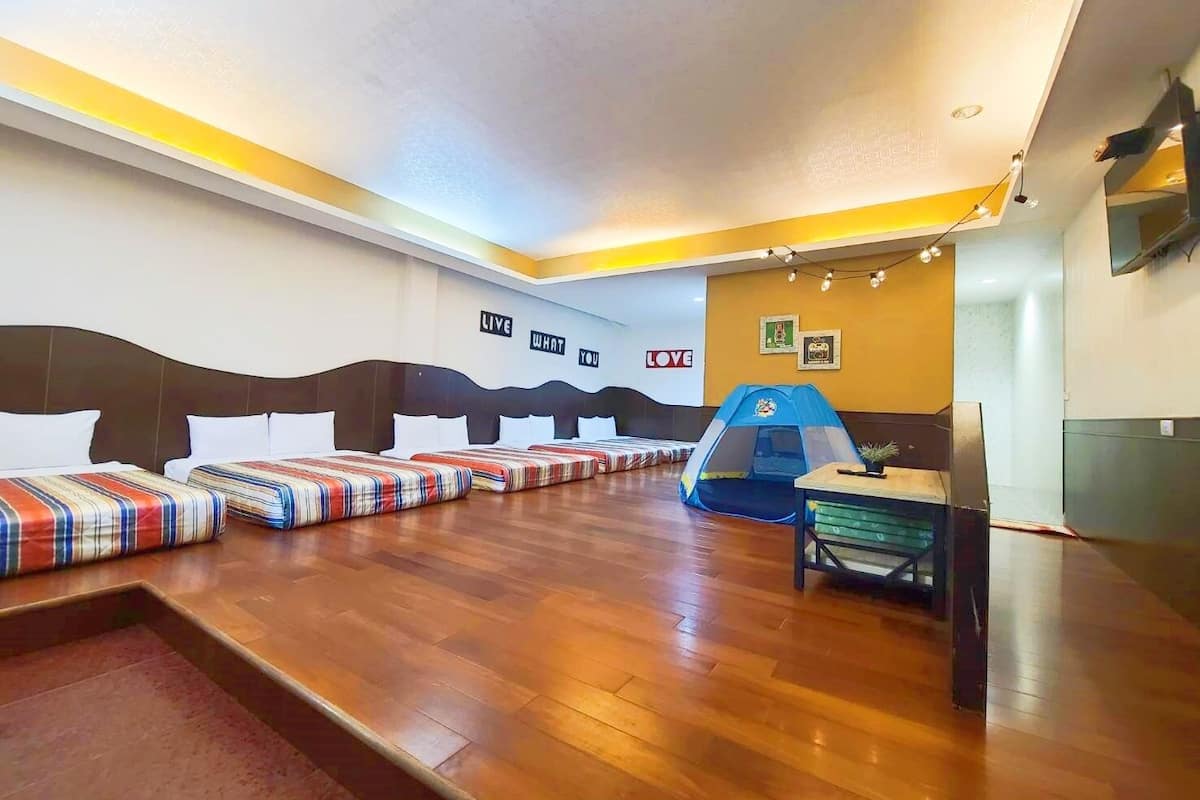 A hotel room with four beds, a play tent, and a small table with a plant.