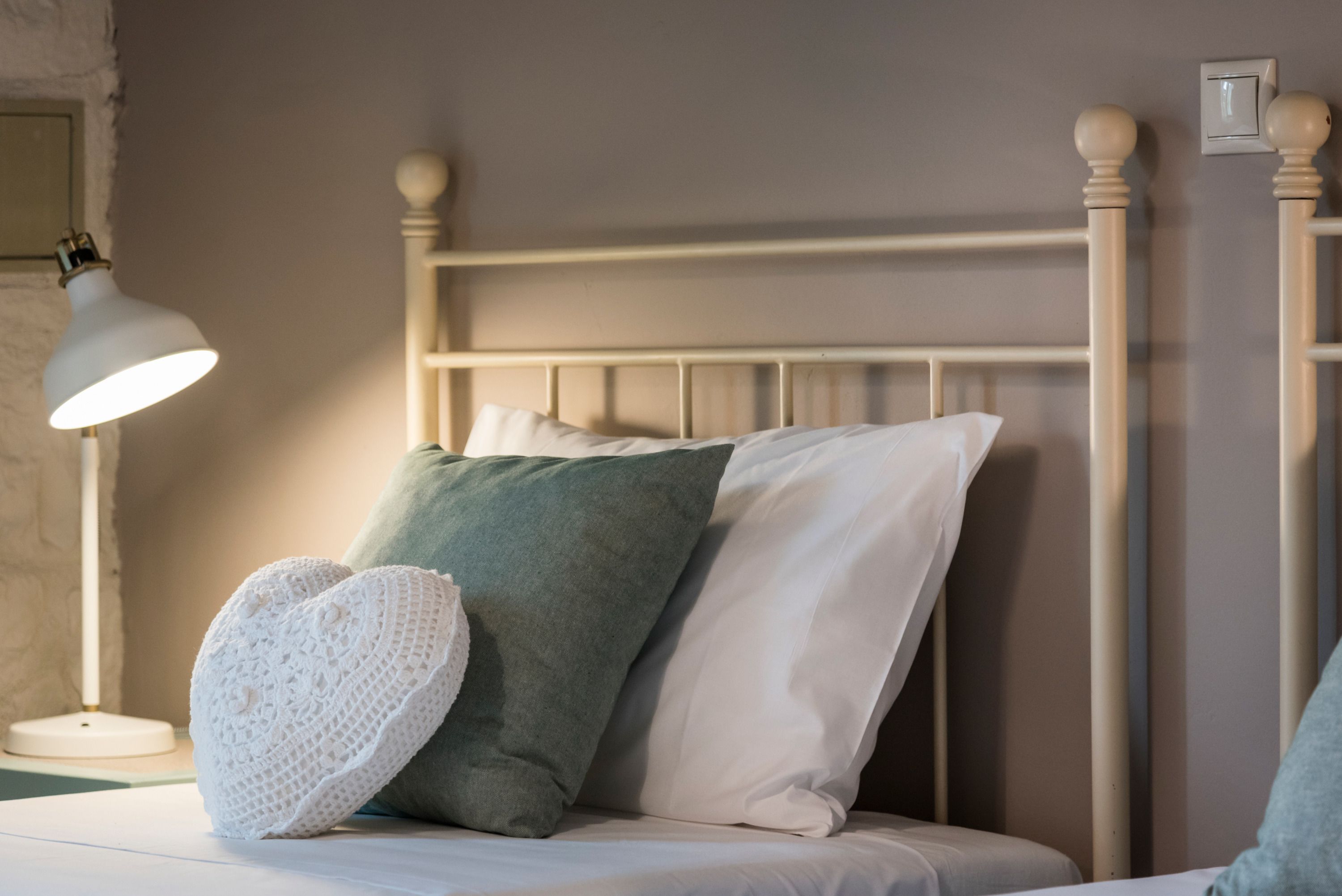 Un lit avec une tête de lit en métal blanche, un oreiller vert, un oreiller blanc et un oreiller blanc en forme de cœur.