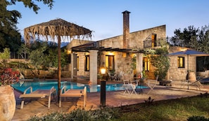 A stone house with a swimming pool, outdoor seating, and a thatched roof structure. - Boutique Villa Petra Amanda (Apokoronas)