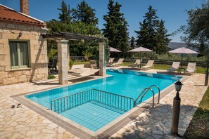 A swimming pool with a stone deck, lounge chairs, and umbrellas.