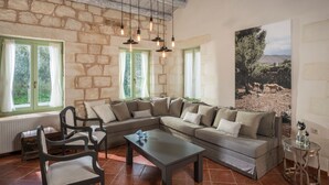 A living room with a stone wall, a sectional sofa, a coffee table, and a painting of a landscape. - Boutique Villa Petra Amanda (Apokoronas)