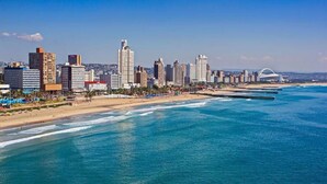 Un paisaje urbano costero con rascacielos, una playa y un puente distintivo.