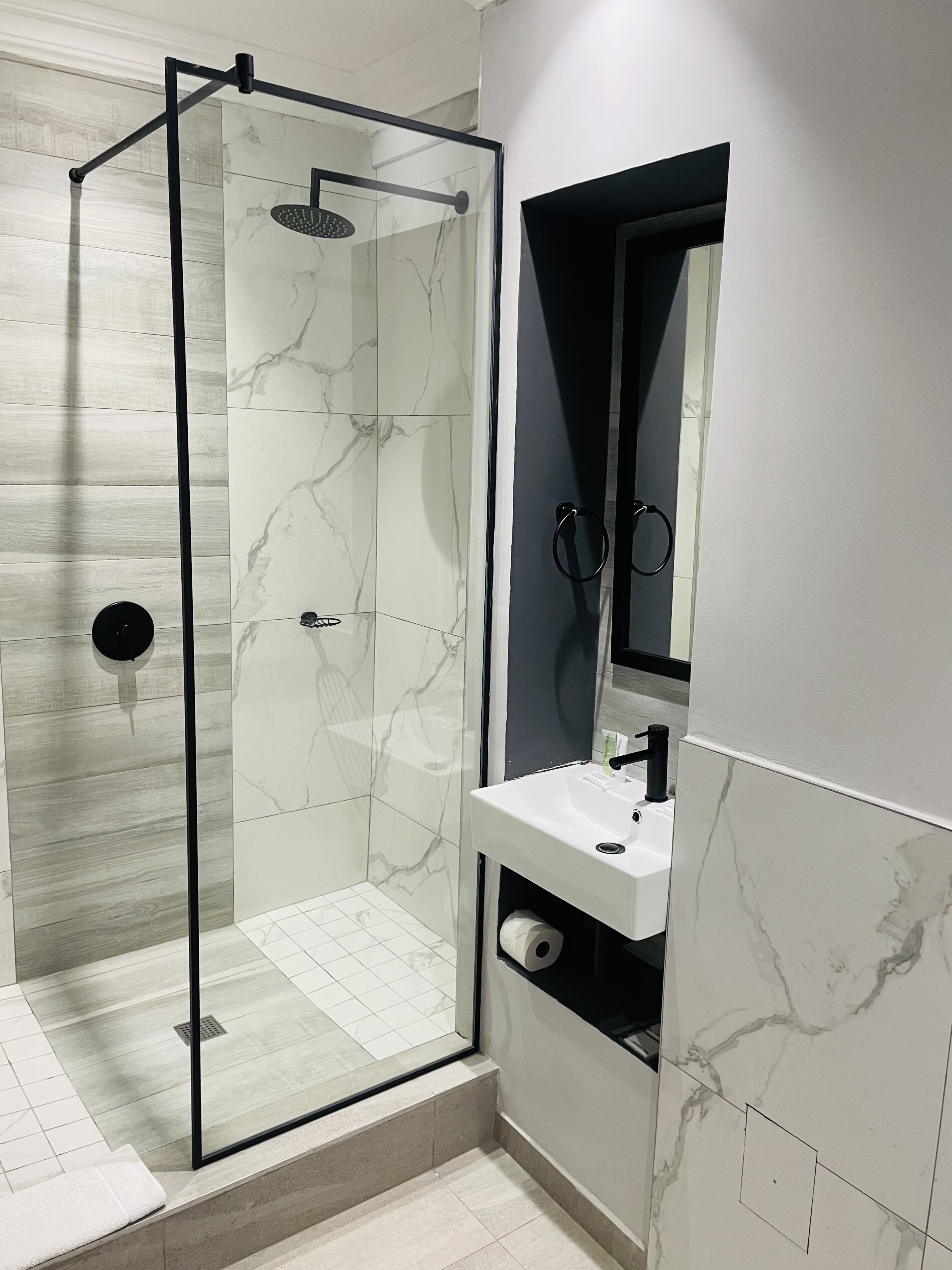 A modern bathroom with a glass-enclosed shower, a white sink with a marble countertop, and a mirror above the sink.