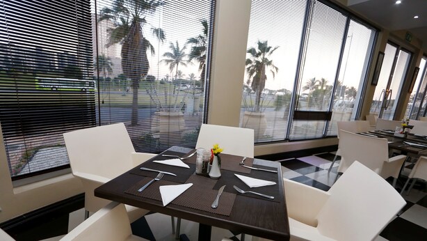 Comedor con una mesa dispuesta para cuatro, sillas blancas y ventanas amplias con persianas.