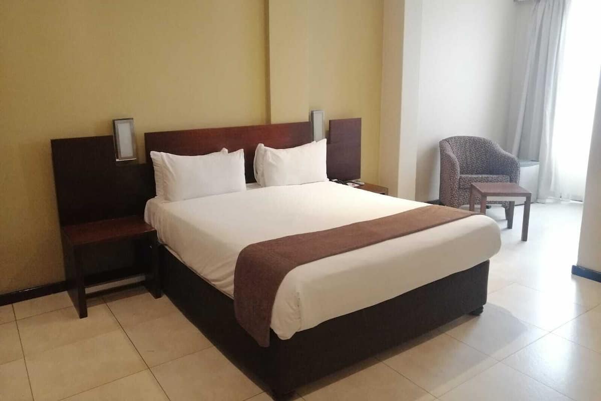 A hotel room with a large bed, a bedside table, a chair, and a window with curtains.