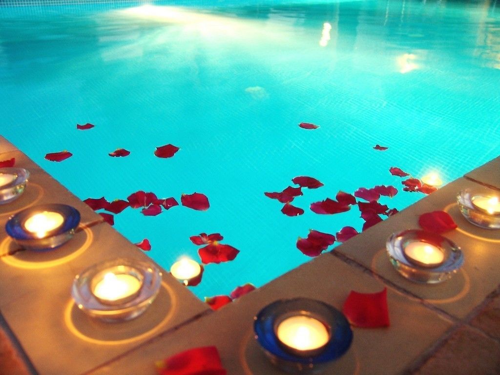 A swimming pool with rose petals and candles on the edge.