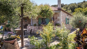 A stone house with a tiled roof, a patio with outdoor furniture, and a garden with various plants and flowers.