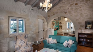 A rustic stone interior with a teal sofa, floral armchair, and a chandelier.