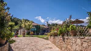 A stone pathway leading to a rustic house with a tiled roof, surrounded by potted plants and a wooden fence.