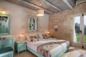 A bedroom with a stone wall, a bed with floral bedding, a nightstand with a lamp, a dresser, and a mirror.