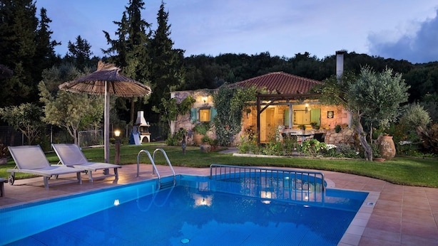 A swimming pool with lounge chairs, a barbecue area, and a stone house with a garden.