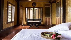 A hotel room with a large bed, a bench, a standing lamp, and a door with a mirror. - Baan Kaew Mongkorn (Hang Dong)