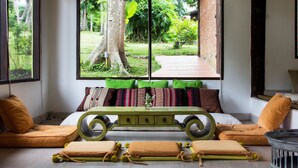 A room with a large window, a bed with multiple pillows, a green table, and a small round table. - Baan Kaew Mongkorn (Hang Dong)