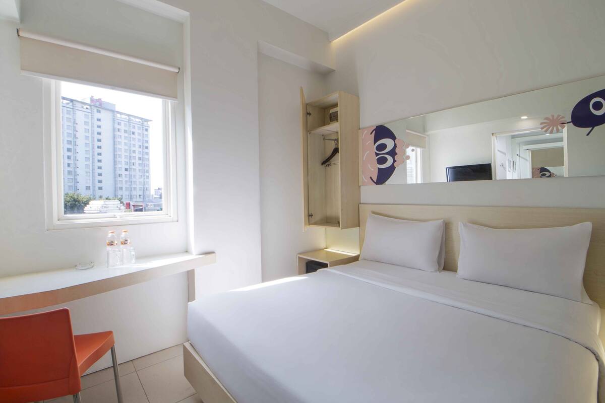 Una habitación de hotel con cama, escritorio, silla, ventana y espejo.