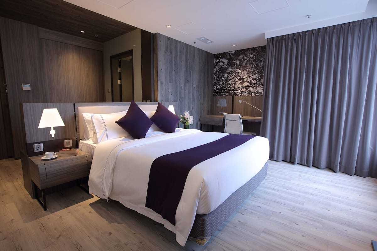 A hotel room with a large bed, bedside tables with lamps, a nightstand, a desk with a chair, and a wall with a floral mural.