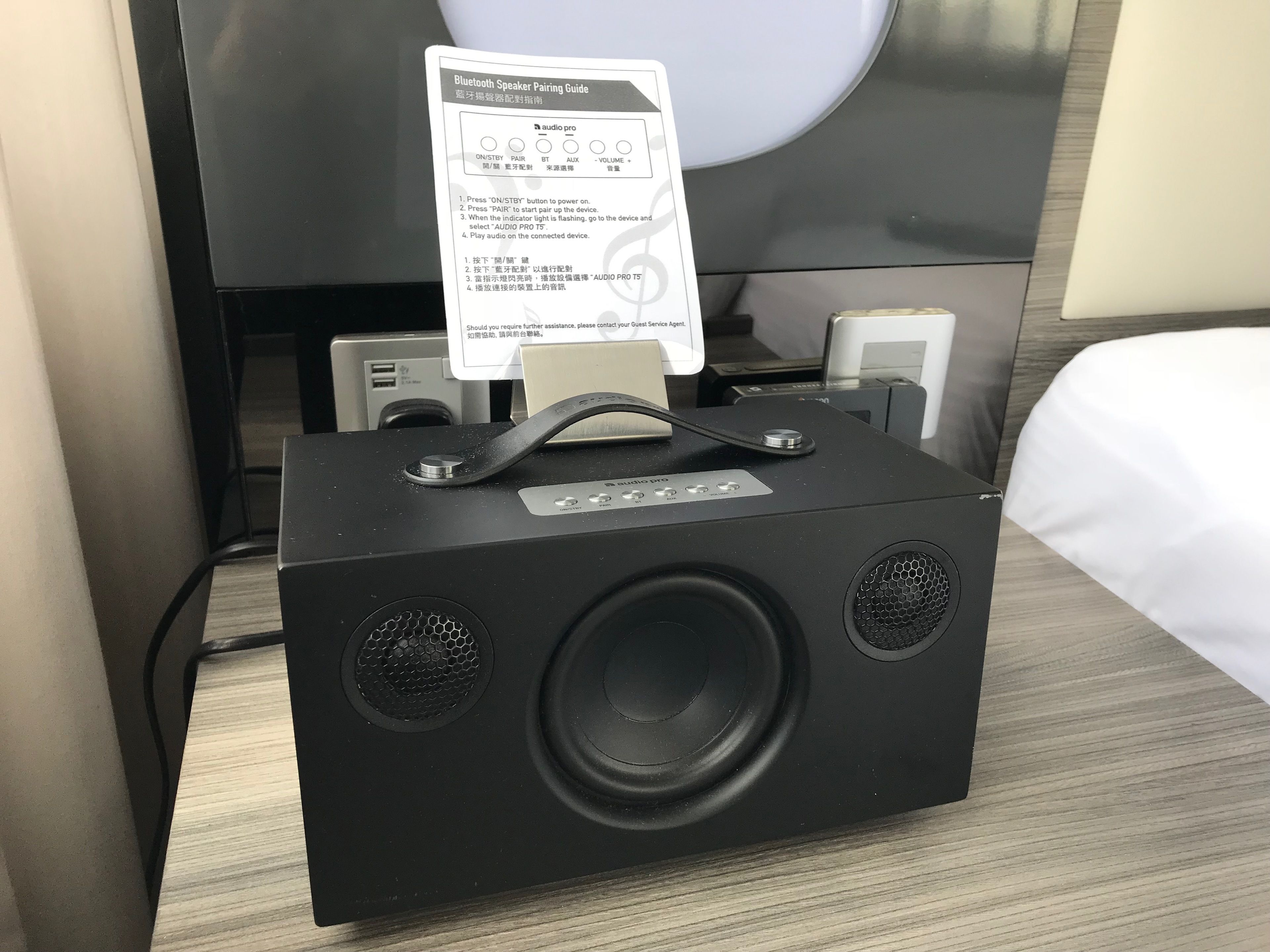 A black portable Bluetooth speaker with a handle, placed on a wooden surface.
