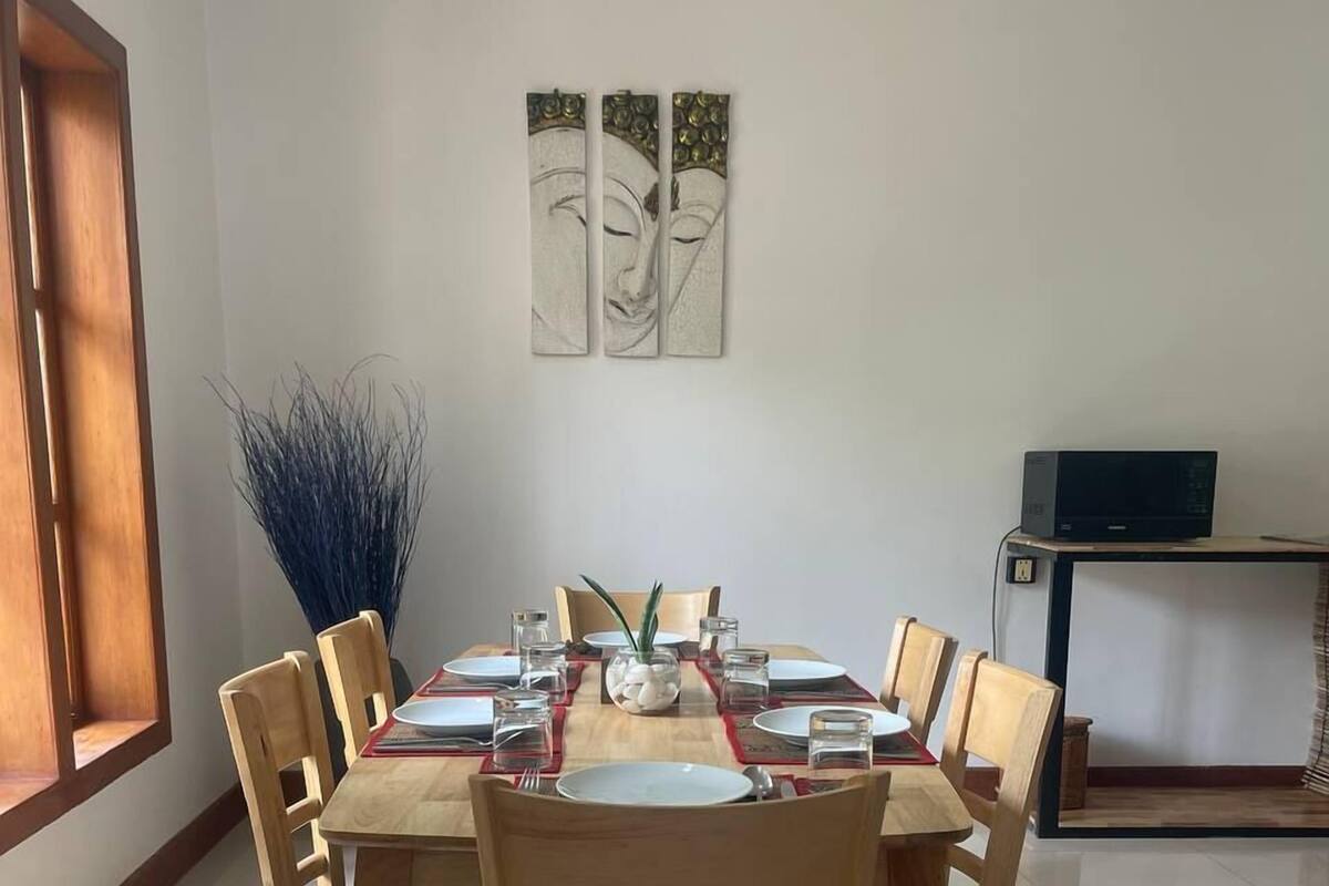 Un coin repas avec une table ronde, des chaises en bois et un four à micro-ondes moderne posé sur une étagère.