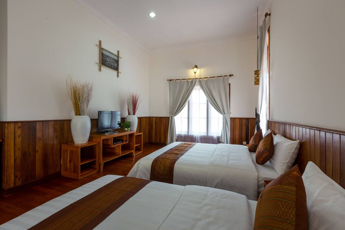 Une chambre d’hôtel avec deux lits, des lambris en bois, un téléviseur posé sur un meuble en bois et une fenêtre avec des rideaux.