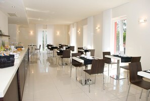 Ein stilvoller Essbereich mit mehreren Tischen und Stühlen, einBuffet mit verschiedenen Speisen und große Fenster, die für natürliches Licht sorgen.