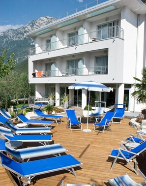 Hotel con zona de piscina que cuenta con sillones azules y sombrillas, rodeado de plantas en macetas y un paisaje montañoso.