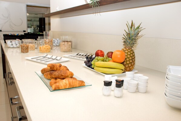 A breakfast buffet with croissants, fruits, and various cereals.
