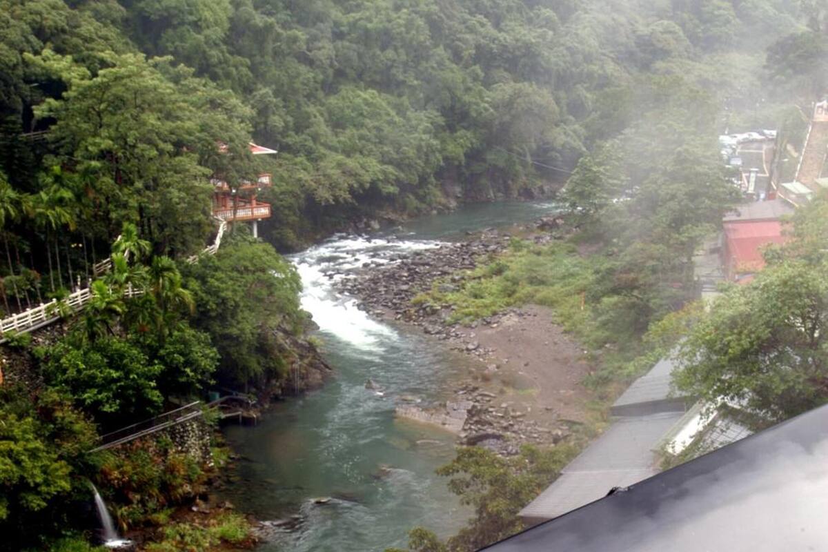Un río que atraviesa una zona boscosa, con un puente y edificios al fondo.