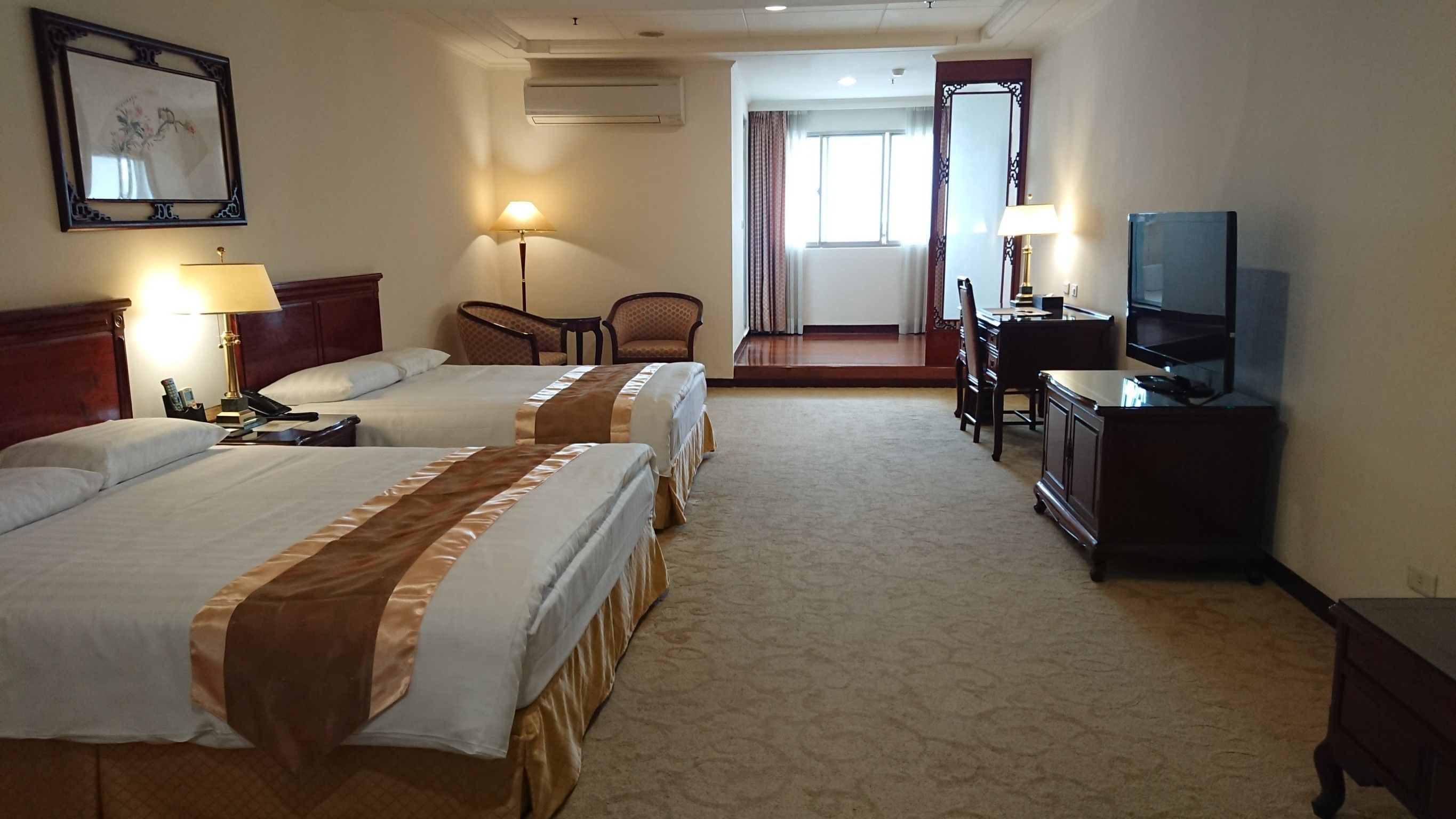A hotel room with two beds, a desk, a chair, a television, and a mirror.