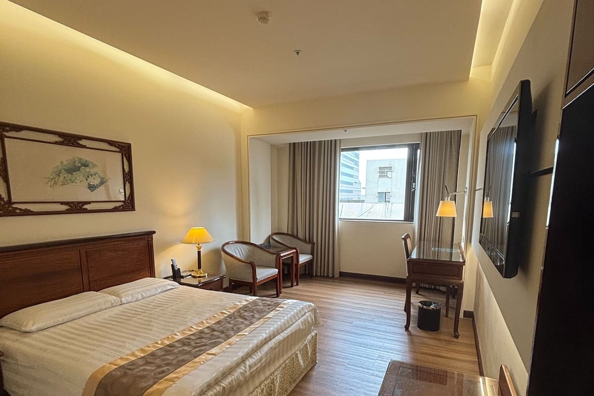 Een hotelkamer met een groot bed, een bureau, een stoel, een televisie en een raam met gordijnen.
