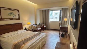 Une chambre d’hôtel avec un grand lit, un bureau, une chaise, une télévision et une fenêtre avec des rideaux.