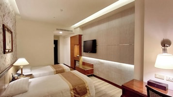 A hotel room with two beds, a TV mounted on the wall, a lamp, and a mirror.