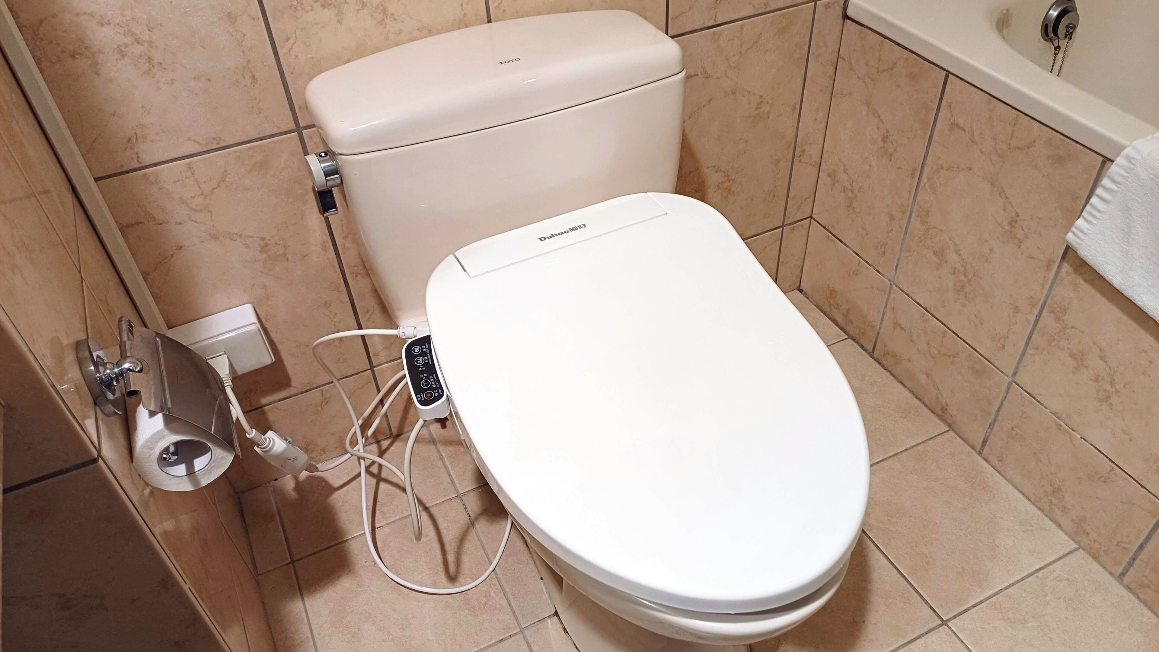 A white toilet with a control panel and a bidet attachment.
