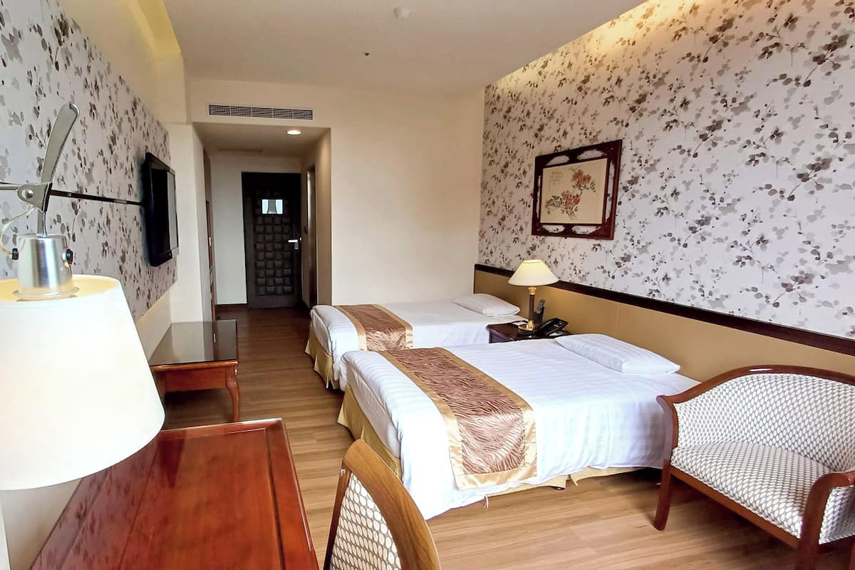 Hotelkamer met twee bedden, een bureau, een stoel, een lamp, een televisie en een ingelijst schilderij aan de muur.
