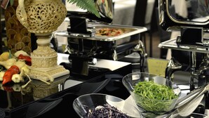 Una mesa de buffet con diversos alimentos y una planta decorativa en un florero tallado.