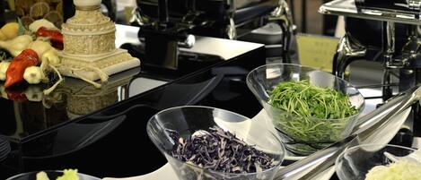 Una mesa de buffet con diversos alimentos y una planta decorativa en un florero tallado.