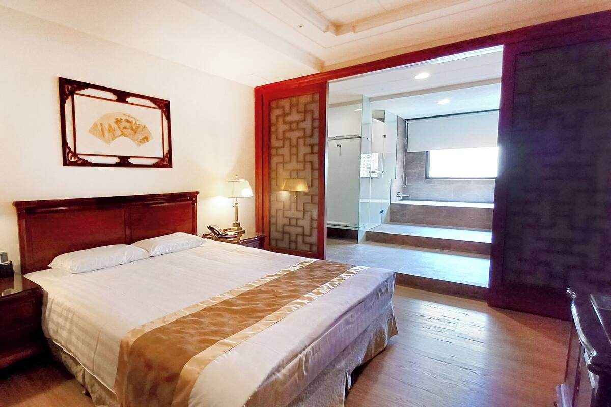 Een hotelkamer met een bed, twee nachtkastjes met lampen, een telefoon aan de muur en een deur naar een badkamer.