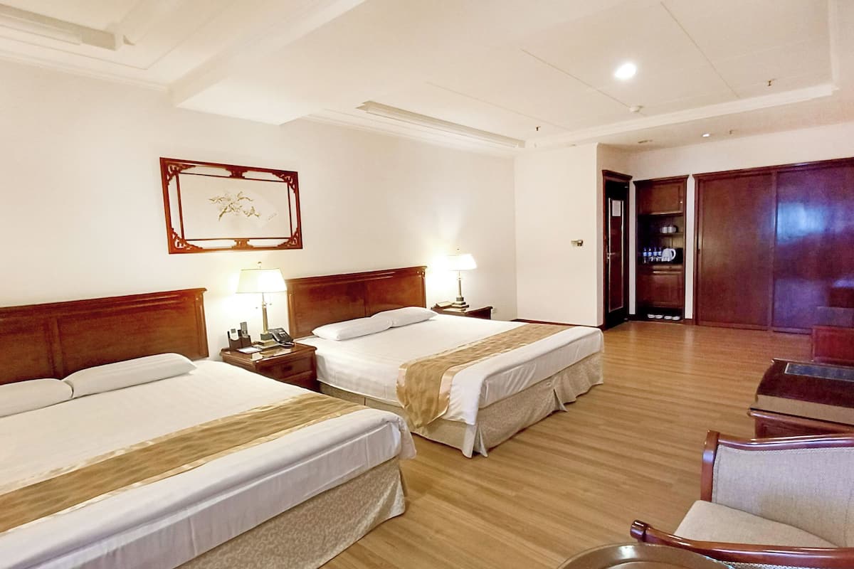 Hotelkamer met twee bedden, een houten vloer, een stoel, een televisie en een deur naar een badkamer.