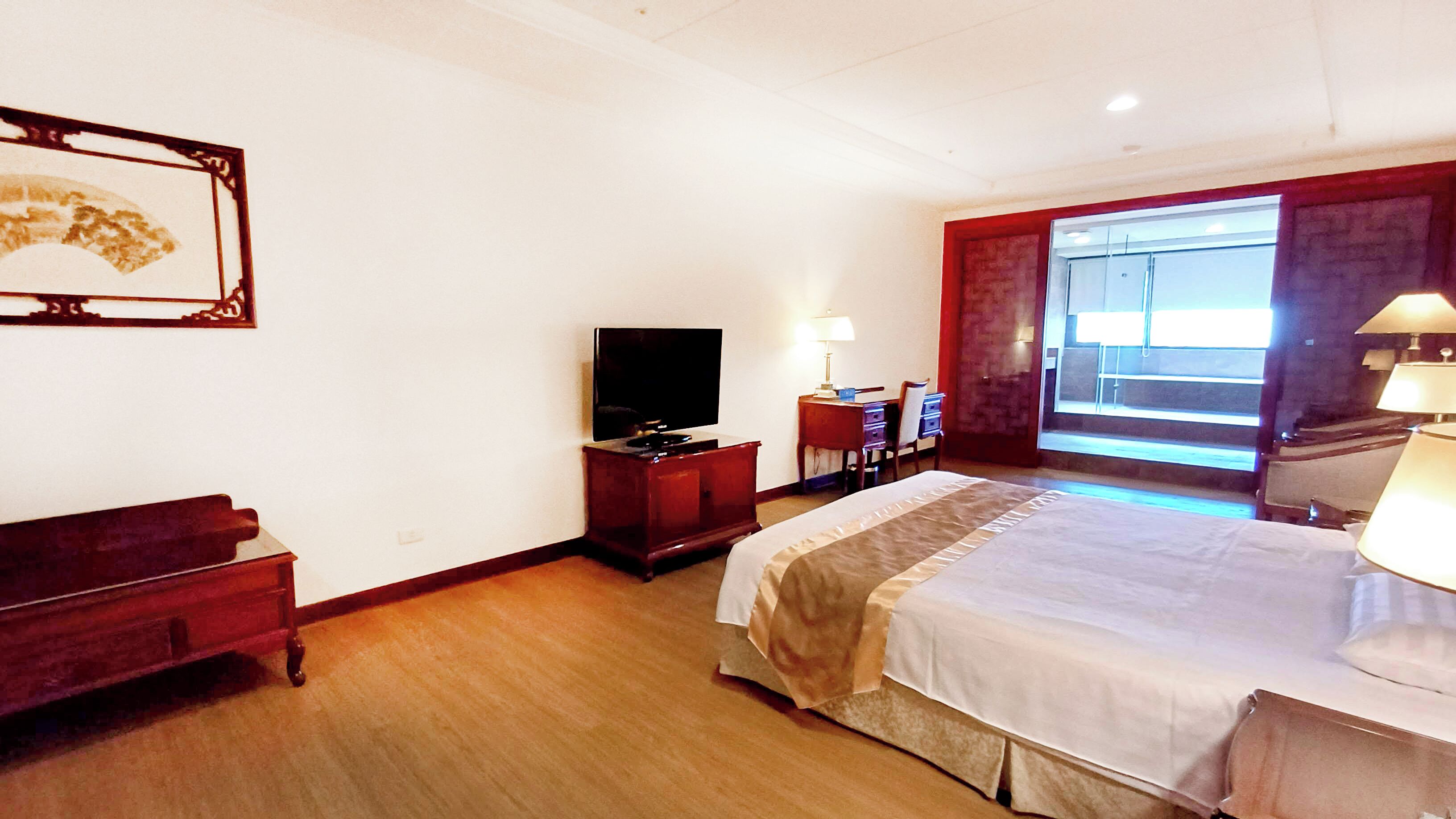 A hotel room with a bed, a television, a desk, and a window with curtains.
