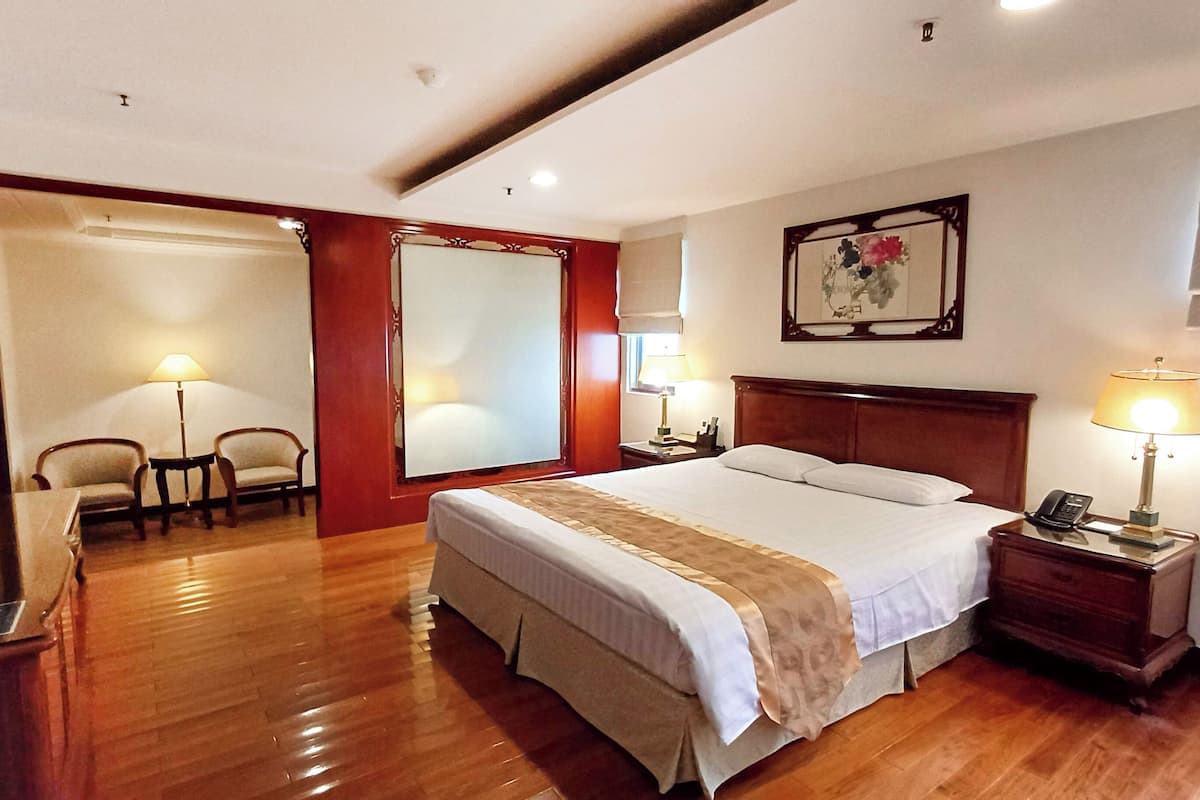 Een hotelkamer met een groot bed, twee nachtkastjes met lampen, een stoel, een bureau, een spiegel en een schilderij aan de muur.