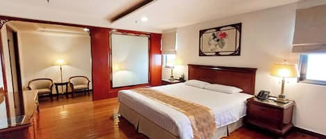 Habitación de hotel con una cama grande, dos mesitas de noche con lámparas, una silla, un escritorio, un espejo y un cuadro en la pared.