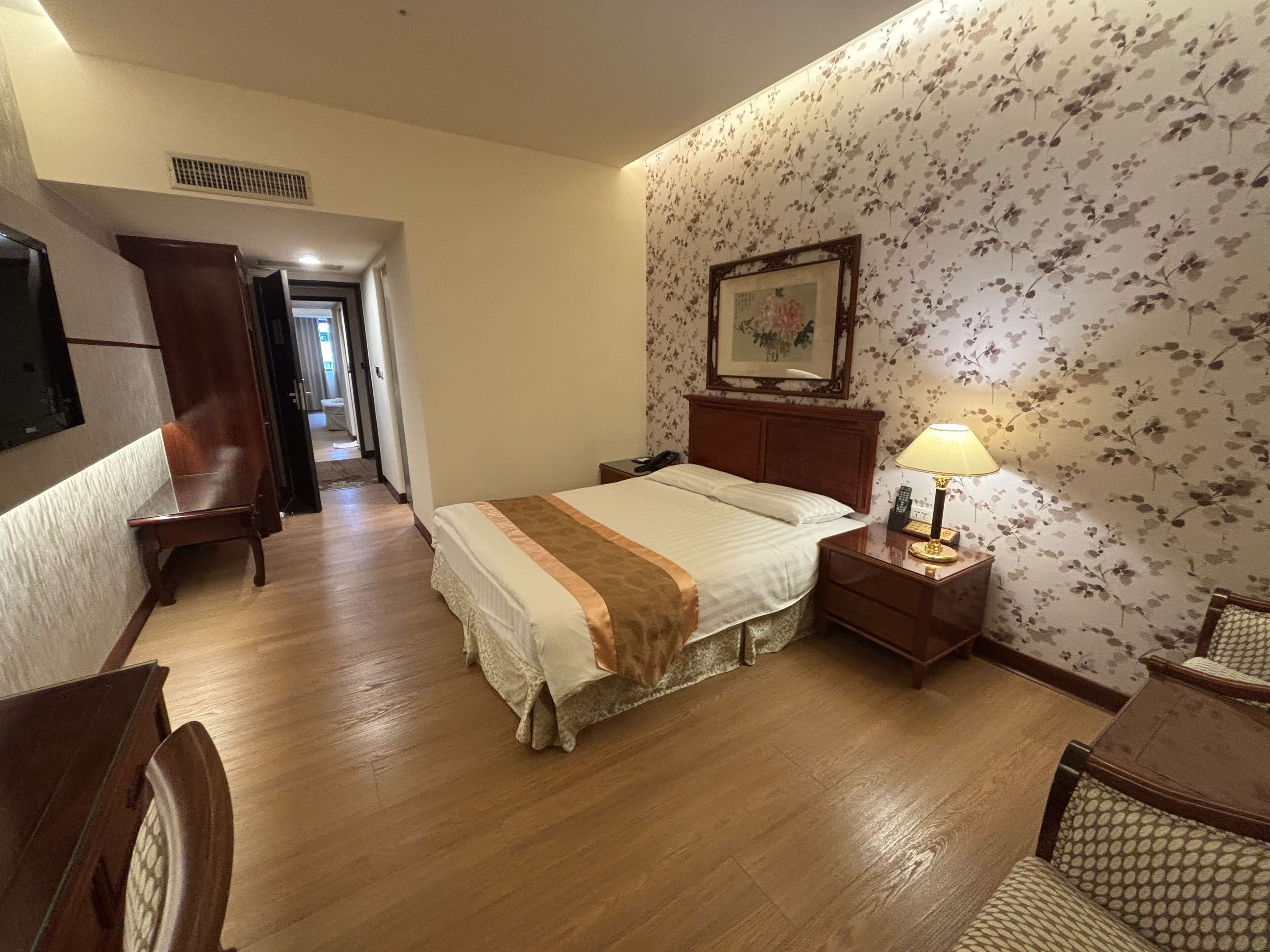 Habitación de hotel con cama, mesita de noche con lámpara, una silla de madera, escritorio y armario.