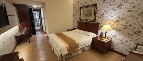 Habitación de hotel con cama, mesita de noche con lámpara, una silla de madera, escritorio y armario.