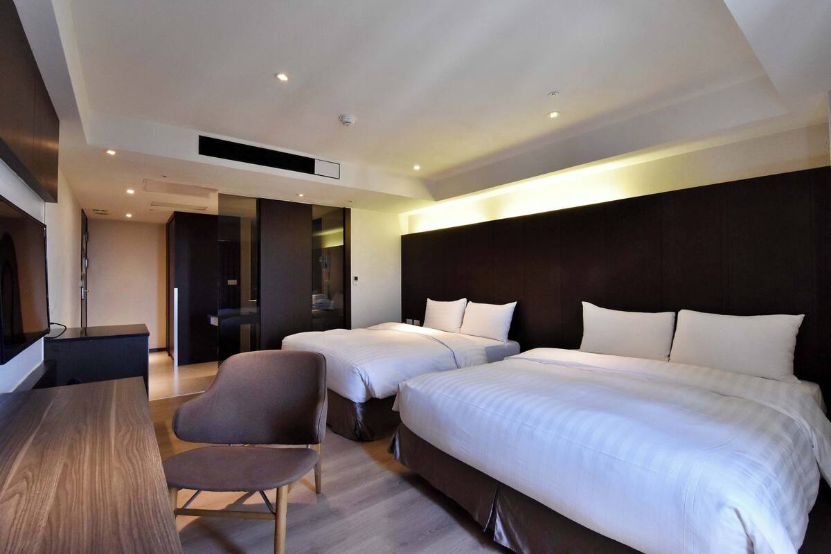 A hotel room with two beds, a desk, and a chair.