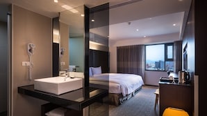 A modern hotel room with a large bed, a bathroom with a sink and hairdryer, a desk with a kettle, and a view of the city through large windows. - Hotel Hi Chuiyang (Chiayi City)