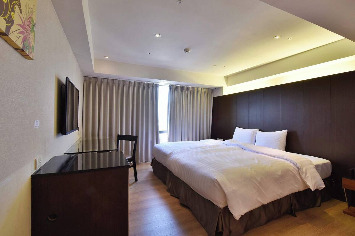 A modern hotel room with a large bed, a desk, and a television.