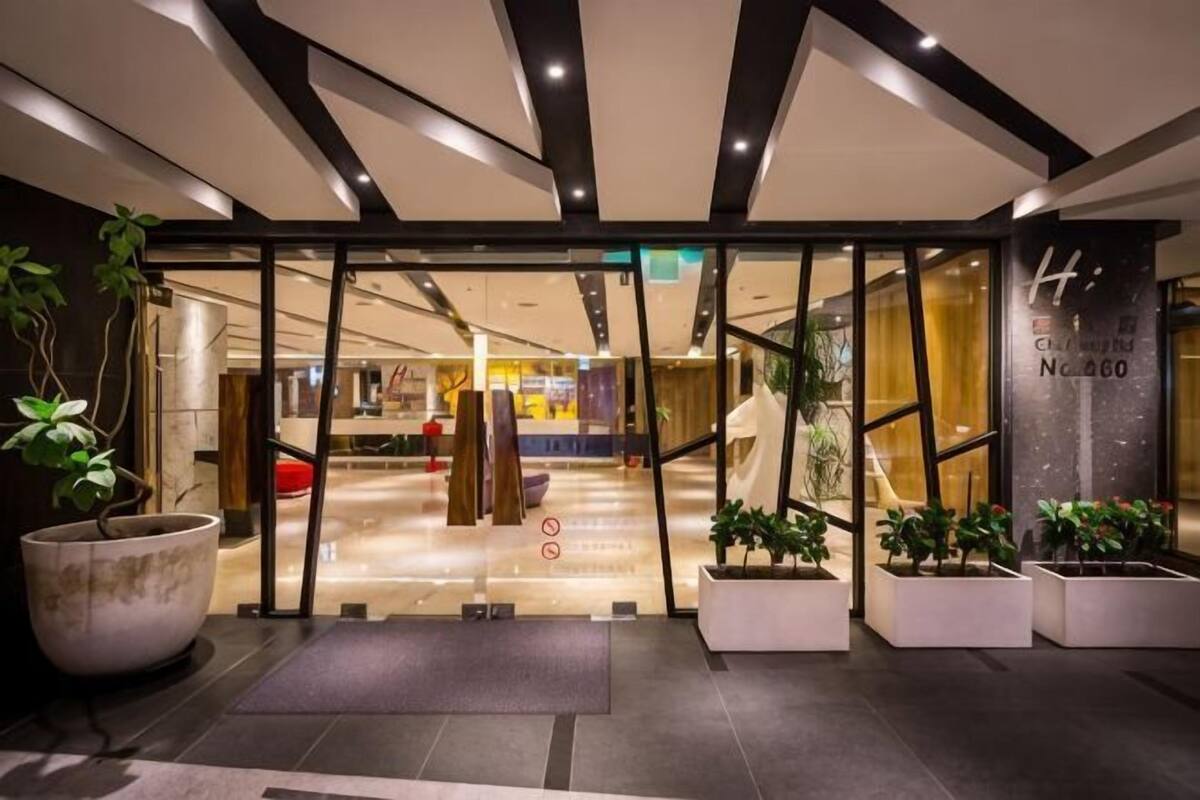 A hotel entrance with a modern design, featuring a glass door, a reception desk, and potted plants.
