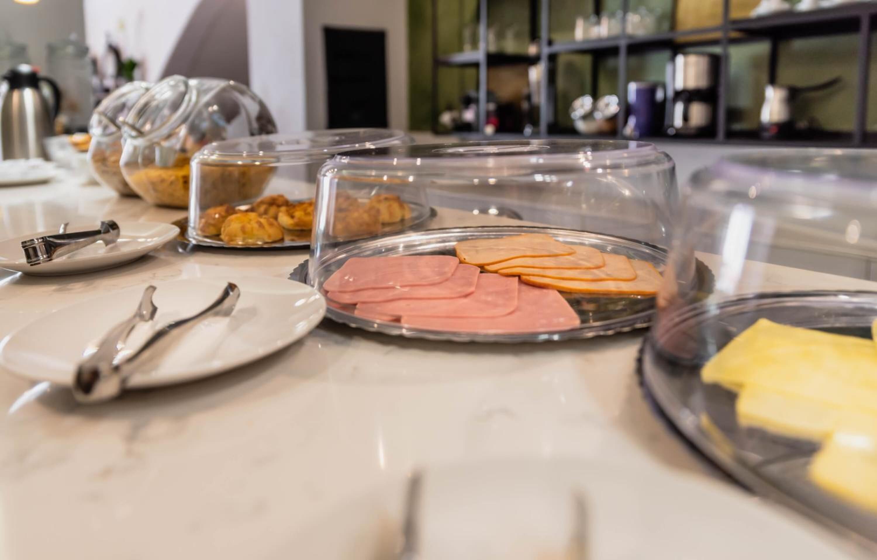 A breakfast buffet with various food items like pastries, ham, and cheese, served in clear glass containers.